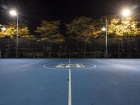 empty tennis court lit up at night with trees in the background and lights on each side