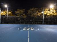 empty tennis court lit up at night with trees in the background and lights on each side