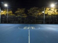 empty tennis court lit up at night with trees in the background and lights on each side