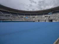 empty tennis court near many chairs in a stadium with an overhead view of the arena