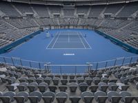 a tennis stadium with empty seats and one court is blue and gray there is no one in the image