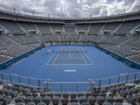 a tennis stadium with empty seats and one court is blue and gray there is no one in the image