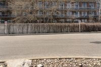 an empty street with rocks next to a row of tall buildings in the background and a large wall in the foreground