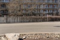 an empty street with rocks next to a row of tall buildings in the background and a large wall in the foreground