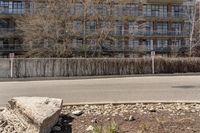 an empty street with rocks next to a row of tall buildings in the background and a large wall in the foreground