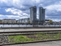 the train tracks beside the river under clouds and sky's are empty, with grass on each side