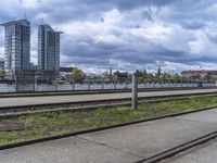 the train tracks beside the river under clouds and sky's are empty, with grass on each side