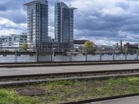 the train tracks beside the river under clouds and sky's are empty, with grass on each side