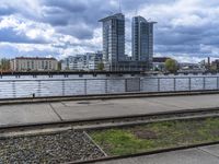 the train tracks beside the river under clouds and sky's are empty, with grass on each side