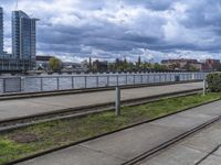 the train tracks beside the river under clouds and sky's are empty, with grass on each side