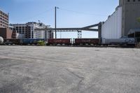 the empty lot of a train yard has two trains in it and an overpass with tracks