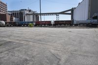 the empty lot of a train yard has two trains in it and an overpass with tracks