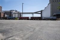 the empty lot of a train yard has two trains in it and an overpass with tracks
