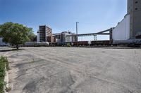 the empty lot of a train yard has two trains in it and an overpass with tracks