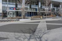 an empty area near buildings is shown with trees in the foreground, and several pedestrians walk on the pavement