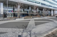 an empty area near buildings is shown with trees in the foreground, and several pedestrians walk on the pavement