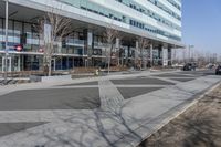 an empty area near buildings is shown with trees in the foreground, and several pedestrians walk on the pavement