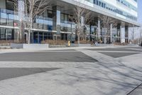 an empty area near buildings is shown with trees in the foreground, and several pedestrians walk on the pavement