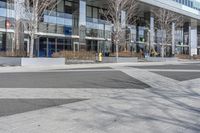 an empty area near buildings is shown with trees in the foreground, and several pedestrians walk on the pavement