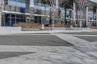 an empty area near buildings is shown with trees in the foreground, and several pedestrians walk on the pavement