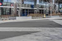 an empty area near buildings is shown with trees in the foreground, and several pedestrians walk on the pavement