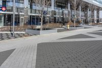 an empty area near buildings is shown with trees in the foreground, and several pedestrians walk on the pavement