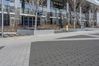 an empty area near buildings is shown with trees in the foreground, and several pedestrians walk on the pavement