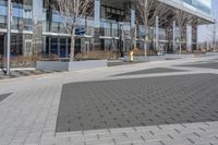 an empty area near buildings is shown with trees in the foreground, and several pedestrians walk on the pavement