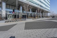 an empty area near buildings is shown with trees in the foreground, and several pedestrians walk on the pavement