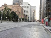 a paved area that is empty and has buildings on both sides of it and cars on the street behind it