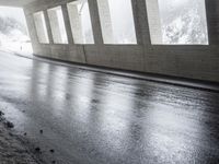 an empty urban road in the rain under a covered bridge of windows and concrete walls