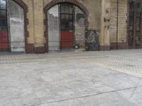 an empty walkway next to a brick building with some graffiti on it and a red door