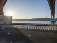 an empty walkway with graffiti in it under the bridge next to a body of water