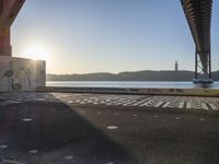 an empty walkway with graffiti in it under the bridge next to a body of water