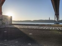 an empty walkway with graffiti in it under the bridge next to a body of water