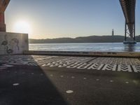 an empty walkway with graffiti in it under the bridge next to a body of water