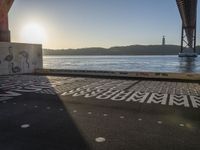 an empty walkway with graffiti in it under the bridge next to a body of water