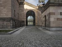 a horse statue and archway at the end of an empty walkway in front of the palace