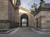 a horse statue and archway at the end of an empty walkway in front of the palace