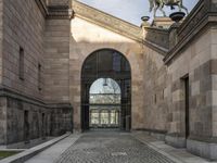 a horse statue and archway at the end of an empty walkway in front of the palace