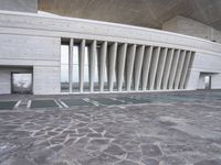 an empty walkway leads to a building with huge white columns that form a structure of arches