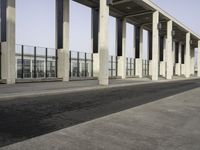 an empty walkway near the parking lot with concrete columns and glass doors, next to a large building with many windows