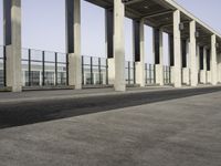 an empty walkway near the parking lot with concrete columns and glass doors, next to a large building with many windows