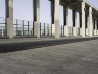 an empty walkway near the parking lot with concrete columns and glass doors, next to a large building with many windows