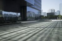 an empty walkway with a reflection in it and some buildings behind it, next to a street