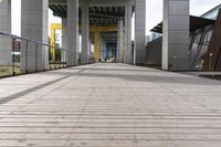 empty walkway next to a street with multiple buildings in the background, and an orange and yellow sign in the middle