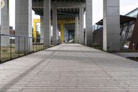 empty walkway next to a street with multiple buildings in the background, and an orange and yellow sign in the middle