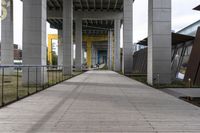 empty walkway next to a street with multiple buildings in the background, and an orange and yellow sign in the middle