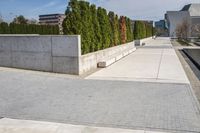the empty concrete walkway leads into a building complex with trees and greenery growing along the wall
