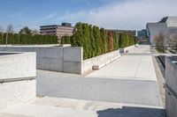 the empty concrete walkway leads into a building complex with trees and greenery growing along the wall